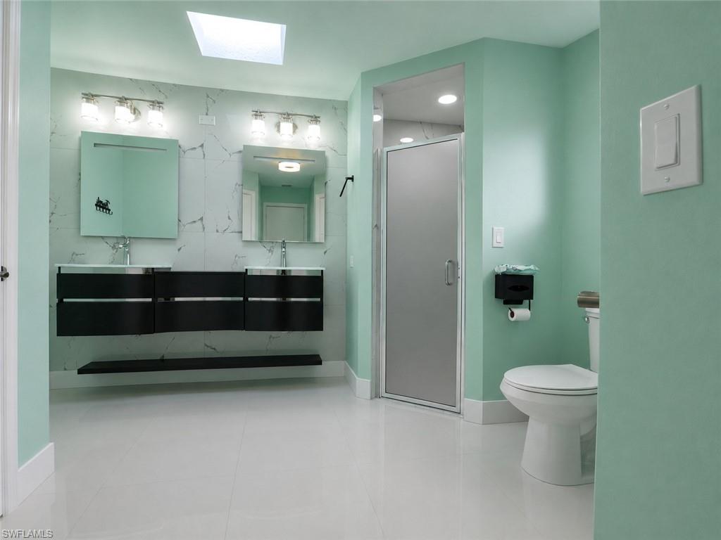 White tile flooring, dual floating vanities, integrated sinks, an enclosed shower, and a skylight