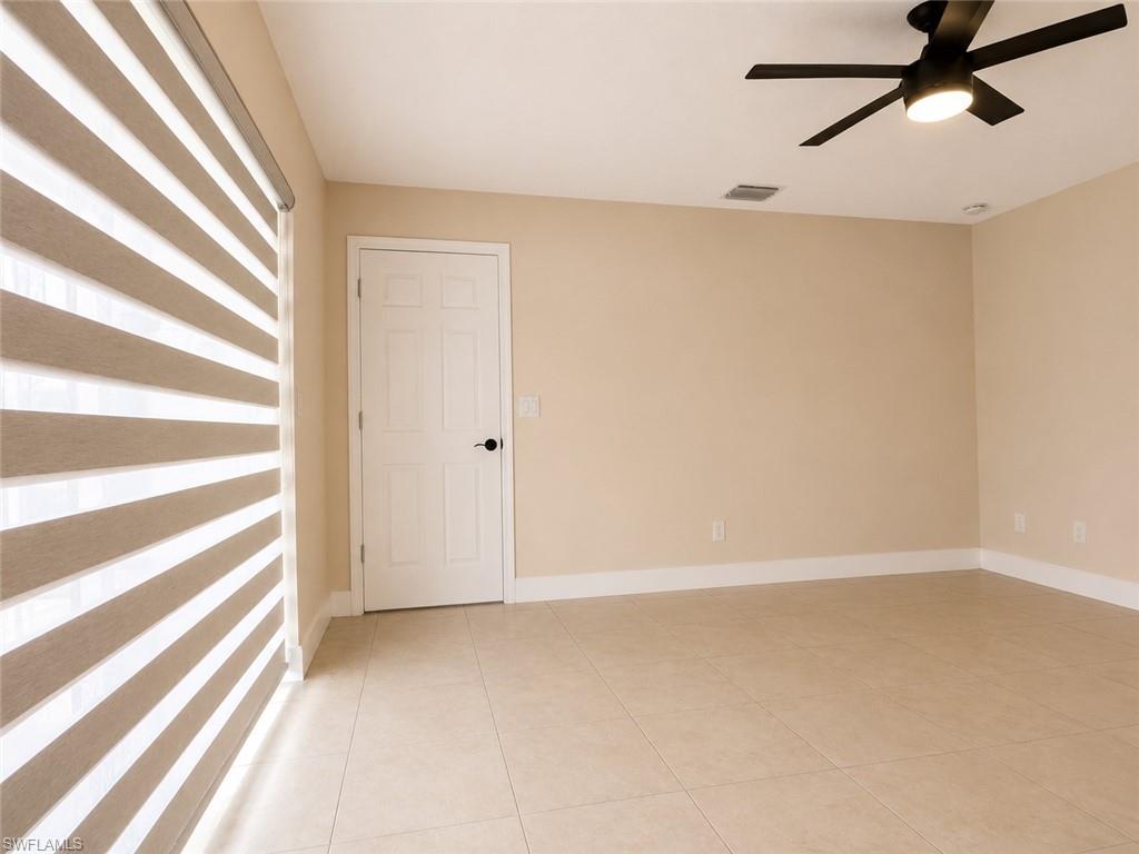 Tile flooring, neutral wall paint, white trim, white paneled door with dark hardware, and a ceiling fan with integrated lighting