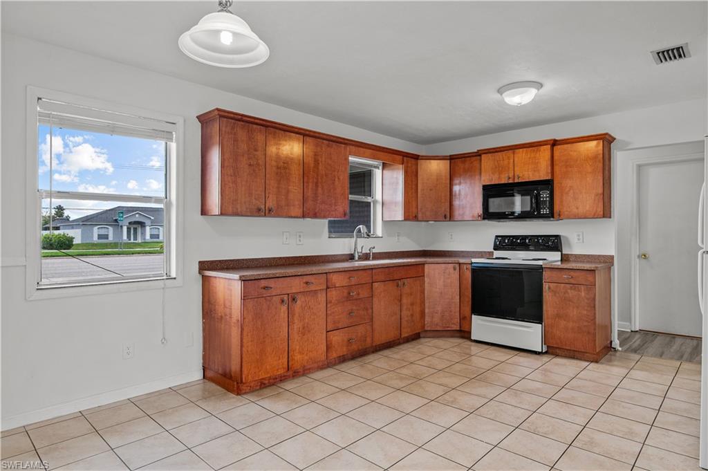 Kitchen with hanging light fixtures, electric stove, sink, and light tile floors