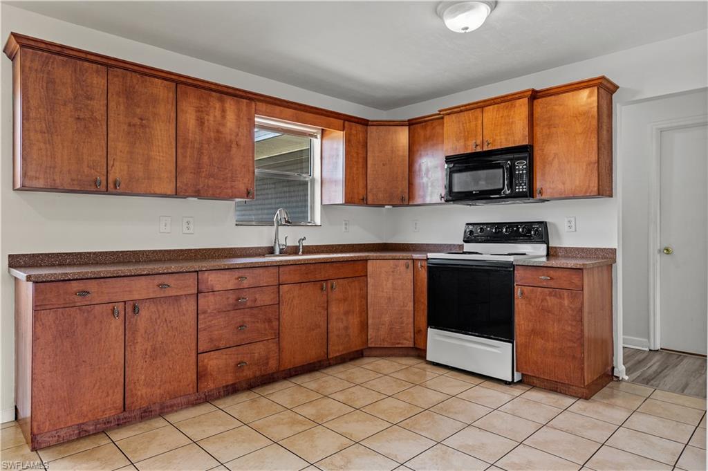 Kitchen with sink, white electric stove and tile flooring