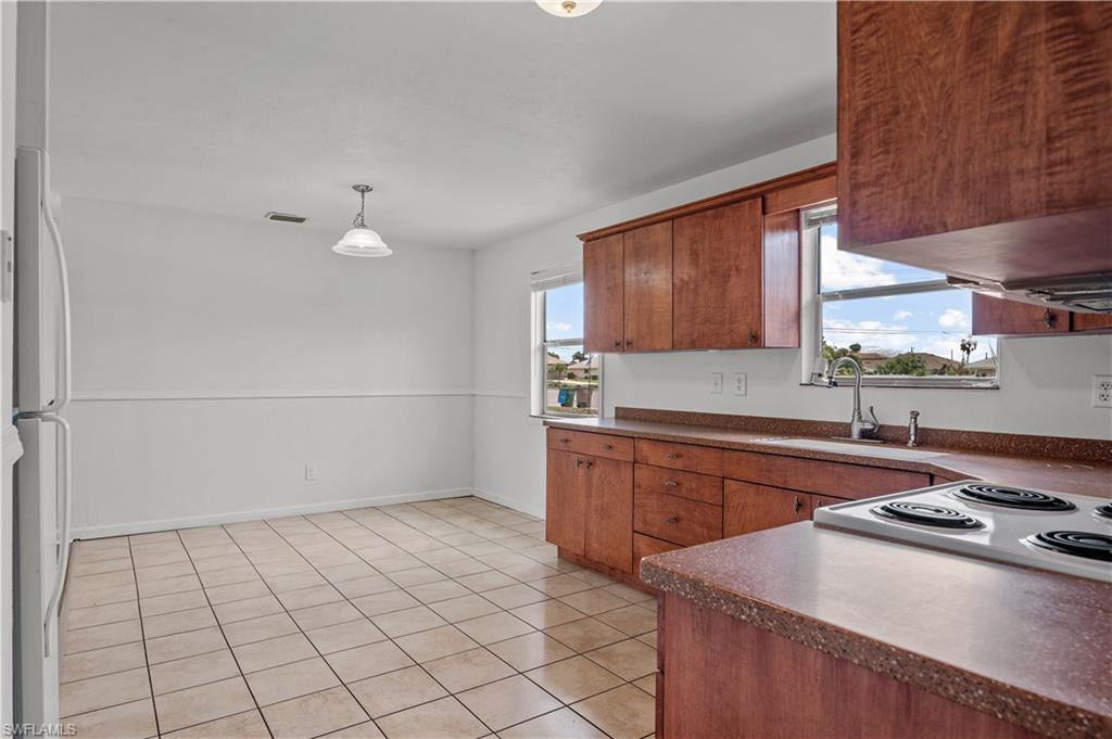 Kitchen with white refrigerator, light tile flooring, pendant lighting, range hood, and sink