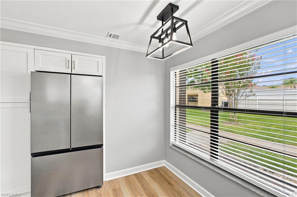 Dedicated refrigerator alcove flanked by premium white cabinetry pantry, a striking modern fixture, and bright window views.