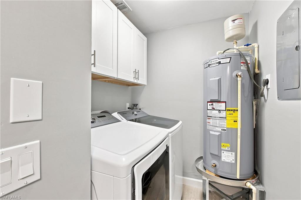 Convenient indoor laundry room comes fully equipped with modern washer and dryer units, built-in storage cabinetry, and an updated water heater.