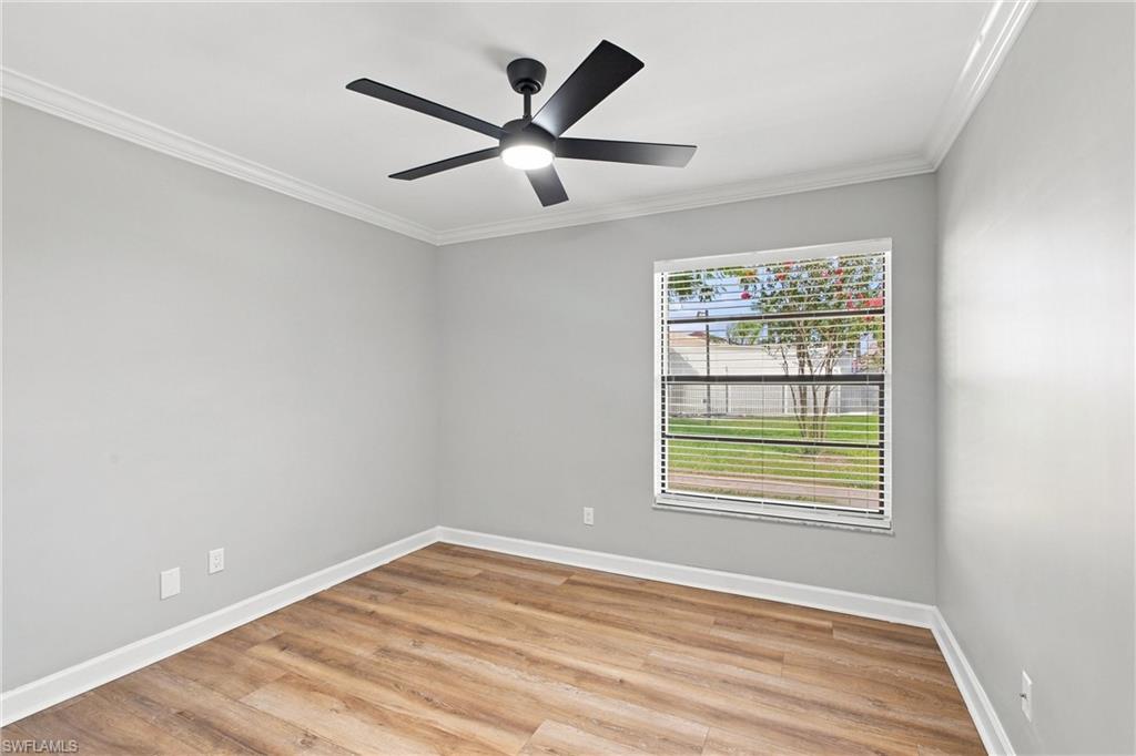Bright second bedroom showcases continuous luxury flooring, fresh modern paint, and a large window streaming in natural light.
