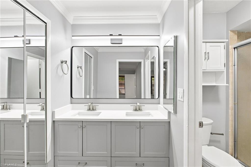 Spa-like primary bathroom features a modern double vanity with quartz countertops, custom grey cabinetry, and an oversized backlit mirror.