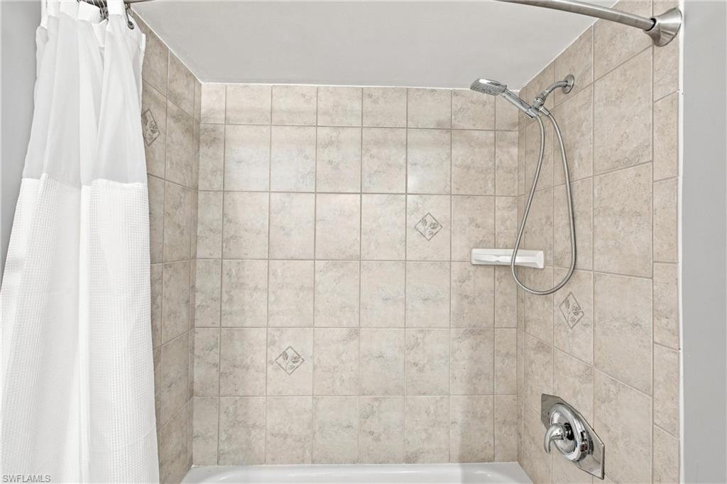 Clean and immaculate second bathroom features a fully tiled tub and shower combination with custom accent inlays and a modern handheld showerhead fixture.