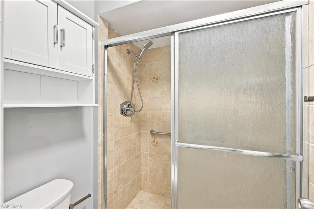 Clean and functional primary bathroom layout includes an over-the-toilet storage cabinet and a fully tiled walk-in shower with sliding glass doors.