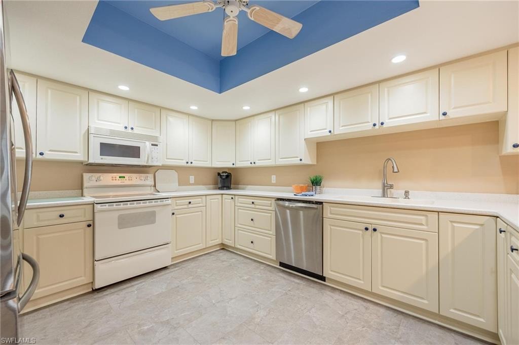 Kitchen featuring light cabinetry, light countertops, integrated stainless steel dishwasher, white range, and a ceiling fan