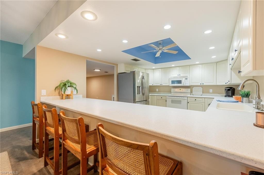 Kitchen featuring a large breakfast bar with solid surface countertops, white cabinetry, recessed lighting, and stainless steel appliances