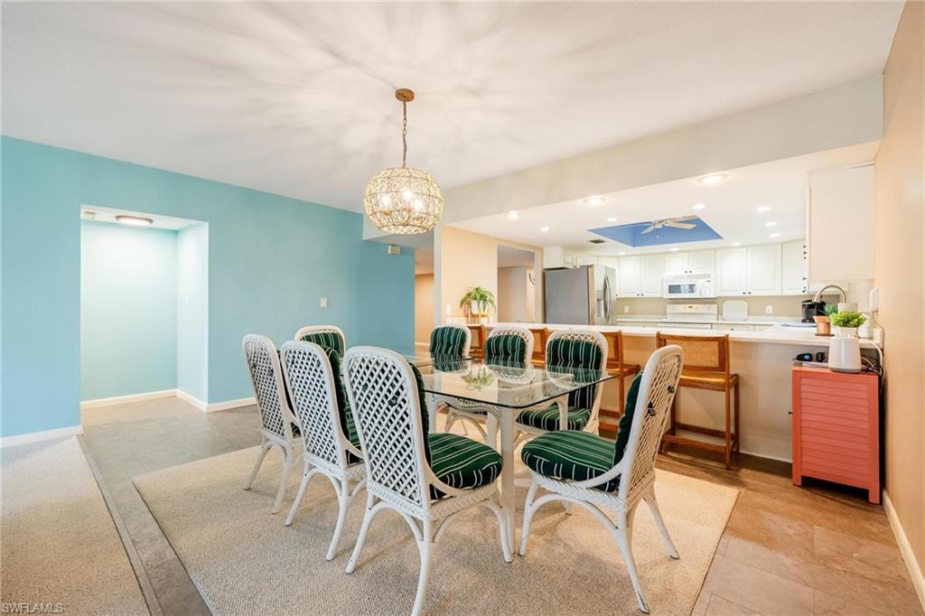 Dining area featuring a glass-top table, white wicker chairs with green striped cushions, and an overhead decorative light fixture