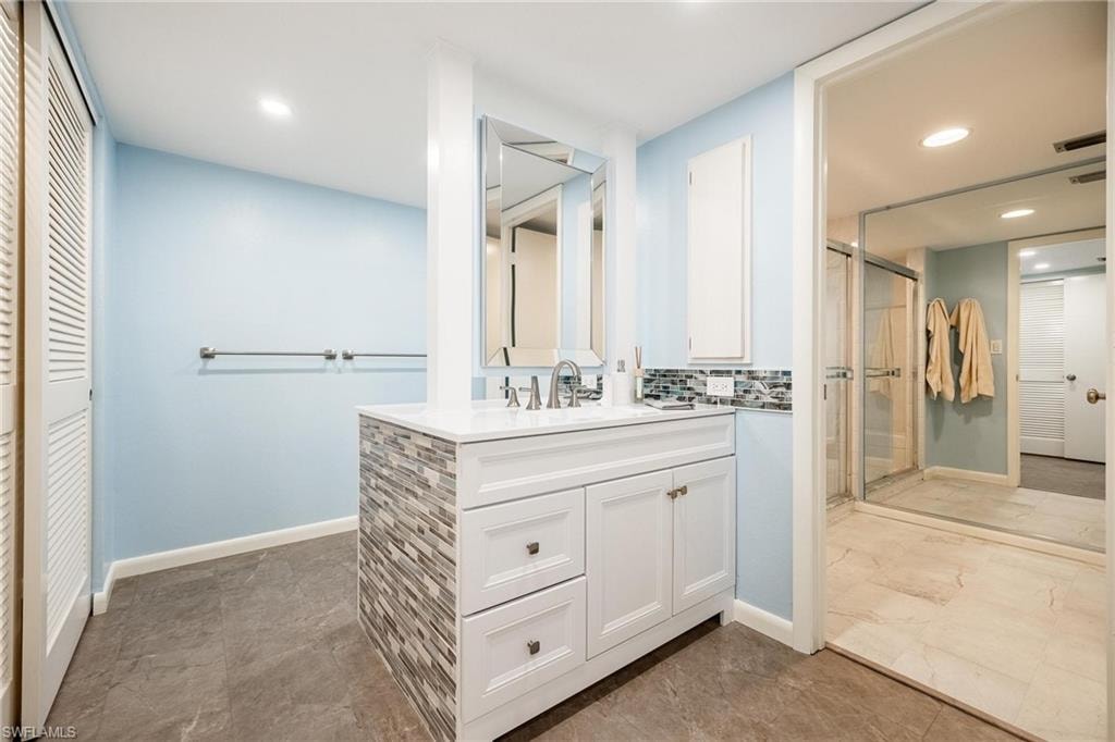Bathroom featuring a contemporary vanity with a white countertop, chrome fixtures, and a stacked stone-look accent panel
