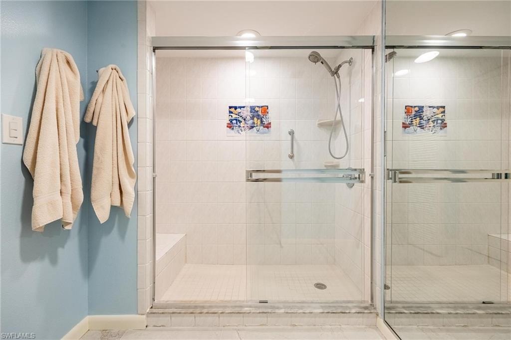 Glass-enclosed shower with white tiled walls and floor, featuring a built-in bench and a wall-mounted shower head