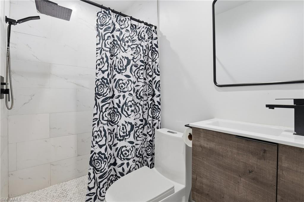 White tiled shower with pebble floor, rain showerhead, black fixtures, and wood-finish vanity with an integrated sink
