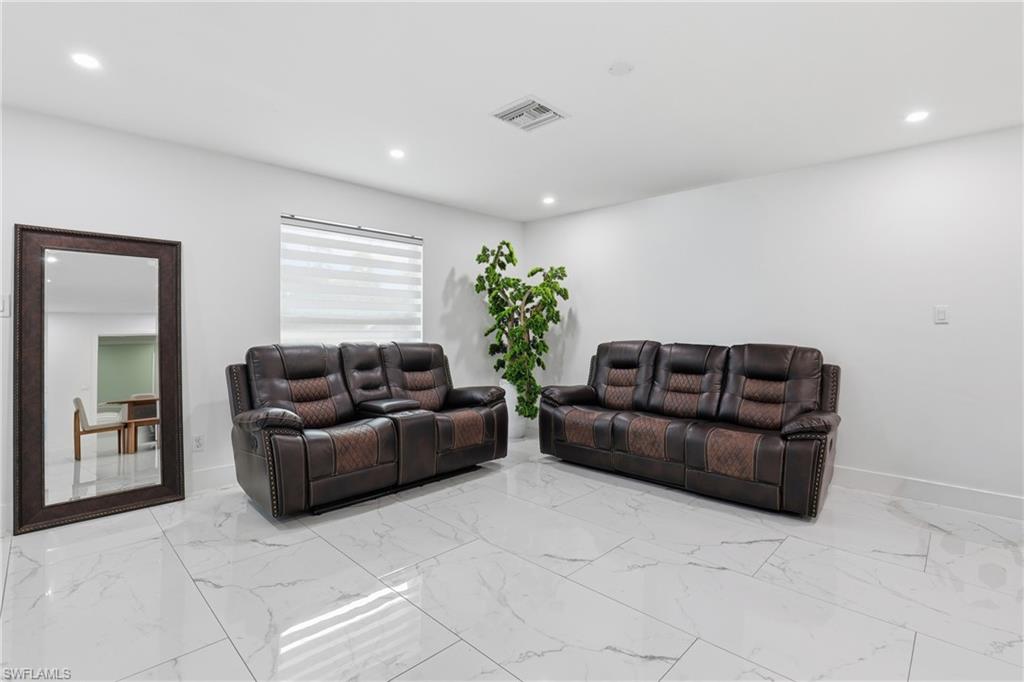 White walls and ceilings with recessed lighting, large rectangular floor tiles, and a window with blinds