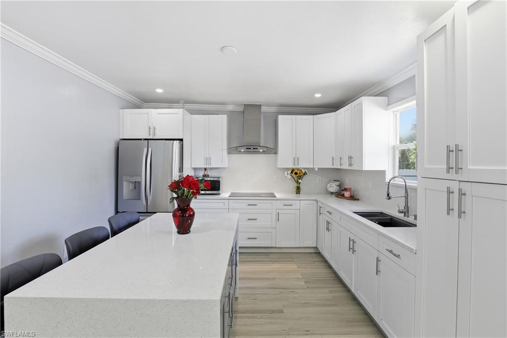 White shaker cabinetry, stainless steel appliances, light-toned wood-finish flooring, quartz countertops, and a kitchen island