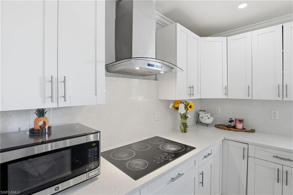 White shaker-style cabinetry with chrome hardware, white speckled countertops, an integrated cooktop, and a stainless steel range hood