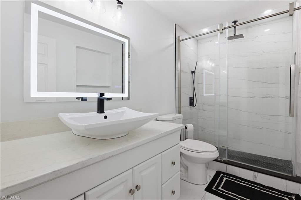 Modern bathroom featuring a rectangular vessel sink with a matte black faucet, an illuminated mirror, a glass-enclosed shower with a rainfall showerhead, and white tile flooring