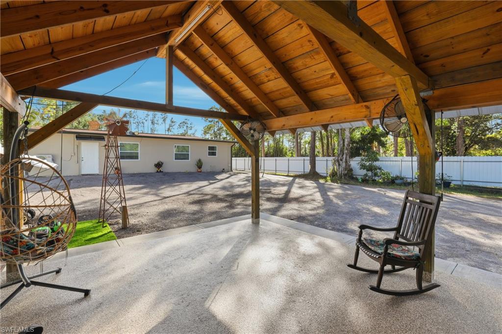 Expansive covered patio with exposed wood beams and ceiling, featuring a textured concrete floor and two attached ceiling fans