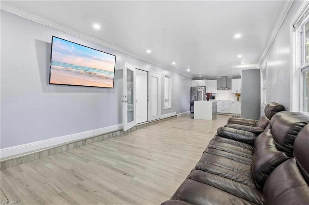 Open-concept living space with wood-finish flooring, recessed lighting, and kitchen with stainless steel appliances and white cabinetry