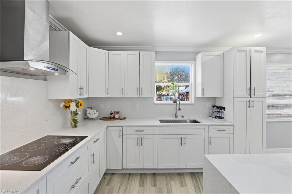 Modern kitchen featuring white shaker cabinetry, light-toned wood-finish flooring, recessed lighting, stainless steel sink, and light-colored countertops