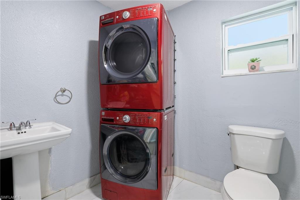 Pedestal sink with chrome faucet, stacked washer and dryer, white window, and toilet