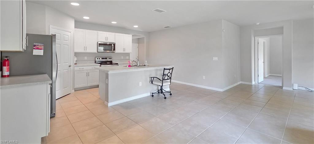 Open-concept kitchen and living area featuring tile flooring, white cabinetry, stainless steel appliances, and an island with a breakfast bar
