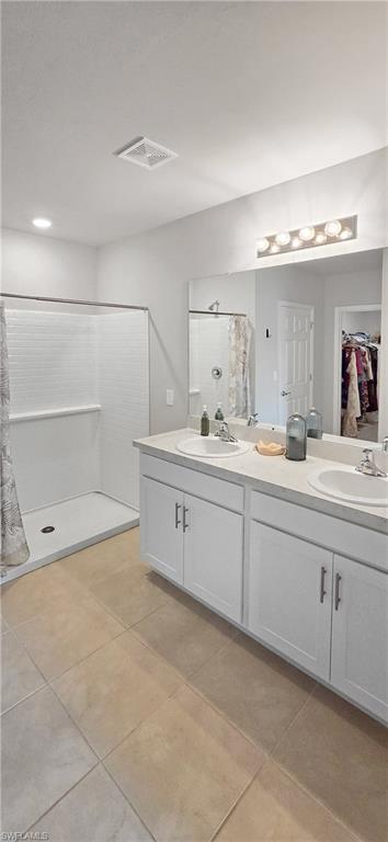 Bathroom featuring a dual vanity with white cabinetry, a large mirror, and a walk-in shower with white tiled walls