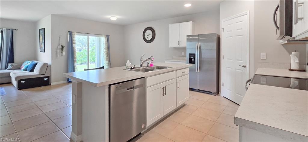 Open-concept kitchen featuring an island with a double basin sink, white cabinetry, stainless steel appliances, and light-toned countertops