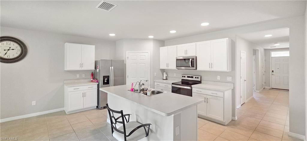 Kitchen featuring a central island with an undermount sink, white cabinetry with silver-tone hardware, stainless steel appliances including a microwave and refrigerator, and recessed lighting