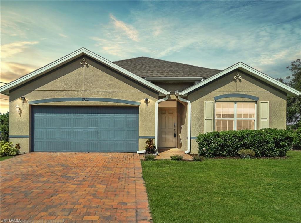 Stucco exterior with a shingle roof, brick paver driveway, attached garage, and manicured landscaping