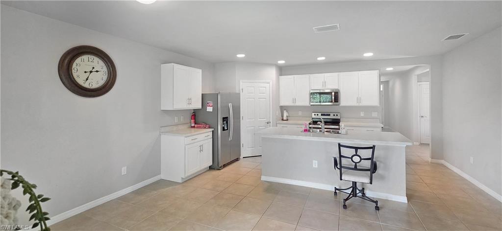 Modern kitchen featuring white cabinetry, light-toned countertops, stainless steel appliances, and a central island with bar seating