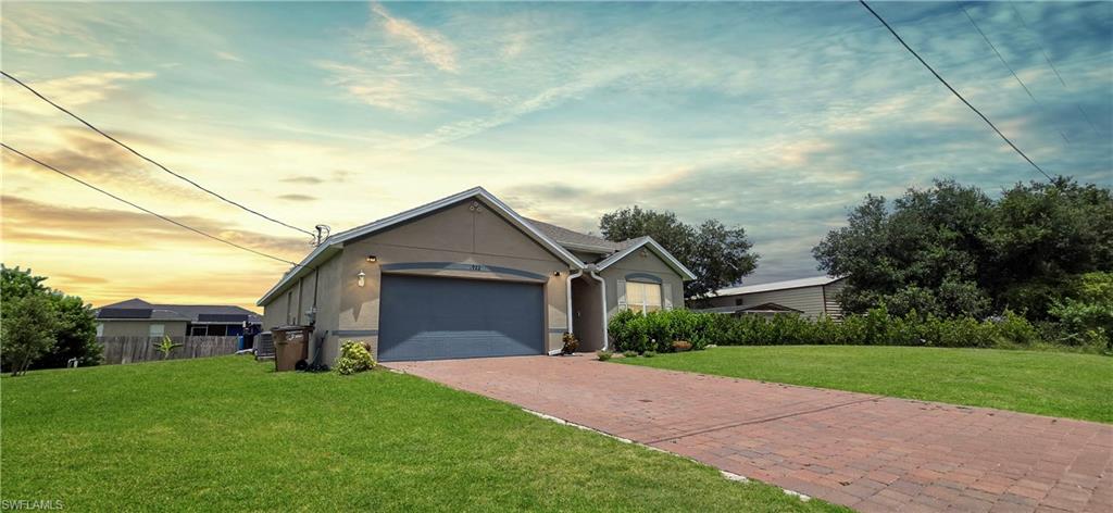 Stucco exterior residence with an attached garage, paver driveway, and manicured front lawn