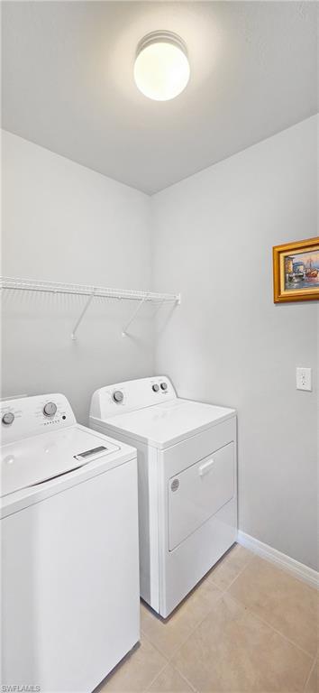 Dedicated laundry space featuring a top-loading washer and front-loading dryer, a wire shelving unit, overhead lighting, and tiled flooring
