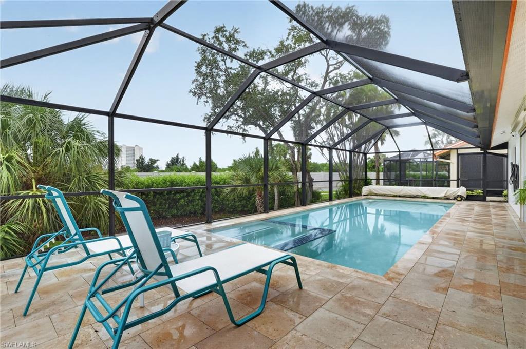 Screened outdoor swimming pool area featuring a rectangular pool, extensive paver decking, and a surrounding privacy hedge