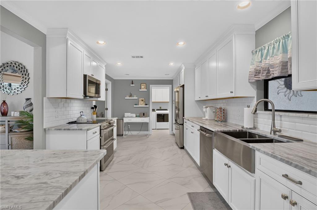 White shaker cabinetry with crown molding, stainless steel appliances, a farmhouse sink with a gooseneck faucet, light-toned countertops, and a subway tile backsplash