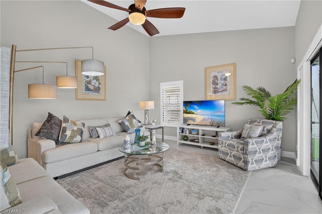 Bright living area featuring vaulted ceilings, a ceiling fan with integrated lighting, and large format tile flooring