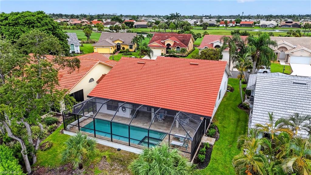 Screened enclosure housing a swimming pool with a paved deck, surrounded by mature landscaping and a terracotta tile roof