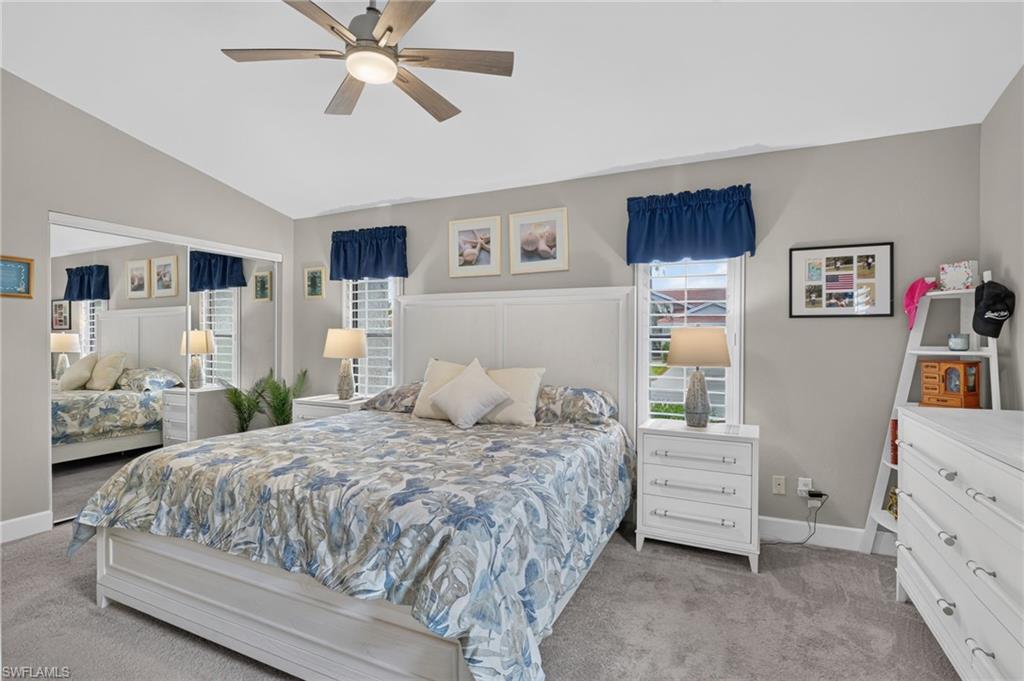 Vaulted ceiling with a ceiling fan, dual windows with plantation shutters, mirrored closet doors, and carpeted flooring