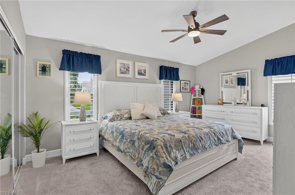 Vaulted ceiling with a ceiling fan, dual windows featuring plantation shutters, neutral-toned carpeting, and mirrored closet doors