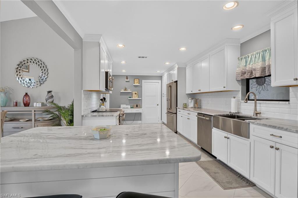 Kitchen featuring a large central island with a stone countertop, white shaker-style cabinetry, and integrated stainless steel appliances