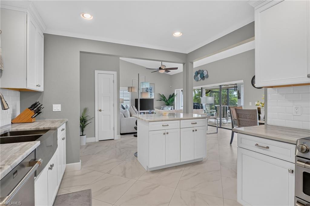 Open-concept kitchen featuring an island, white shaker cabinetry, light-toned countertops, tile flooring, and stainless steel appliances