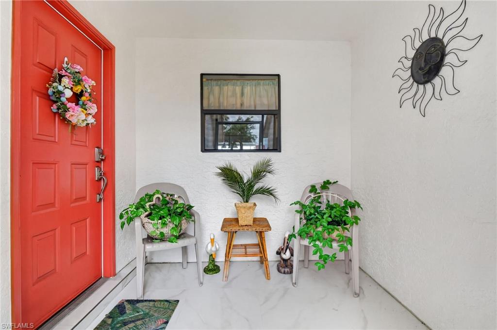Inviting entryway featuring a paneled red door with dark hardware, white stucco walls, and light-toned flooring