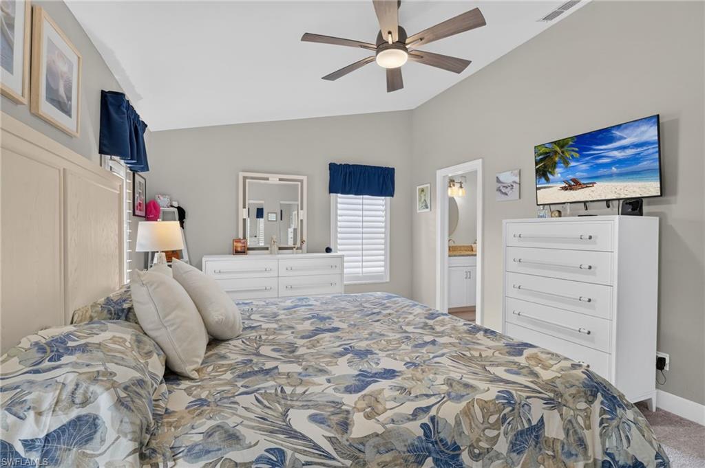 Vaulted ceiling with a ceiling fan, window with plantation shutters, light gray wall paint, and carpet flooring