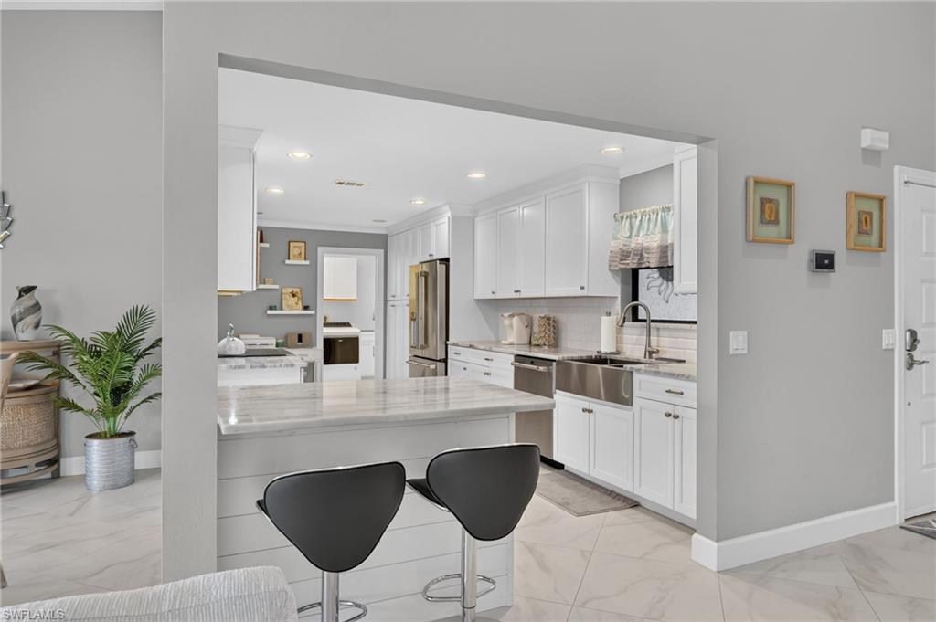 Open-concept kitchen with white cabinetry, stainless steel appliances, a farmhouse sink, and a breakfast bar with stone countertops