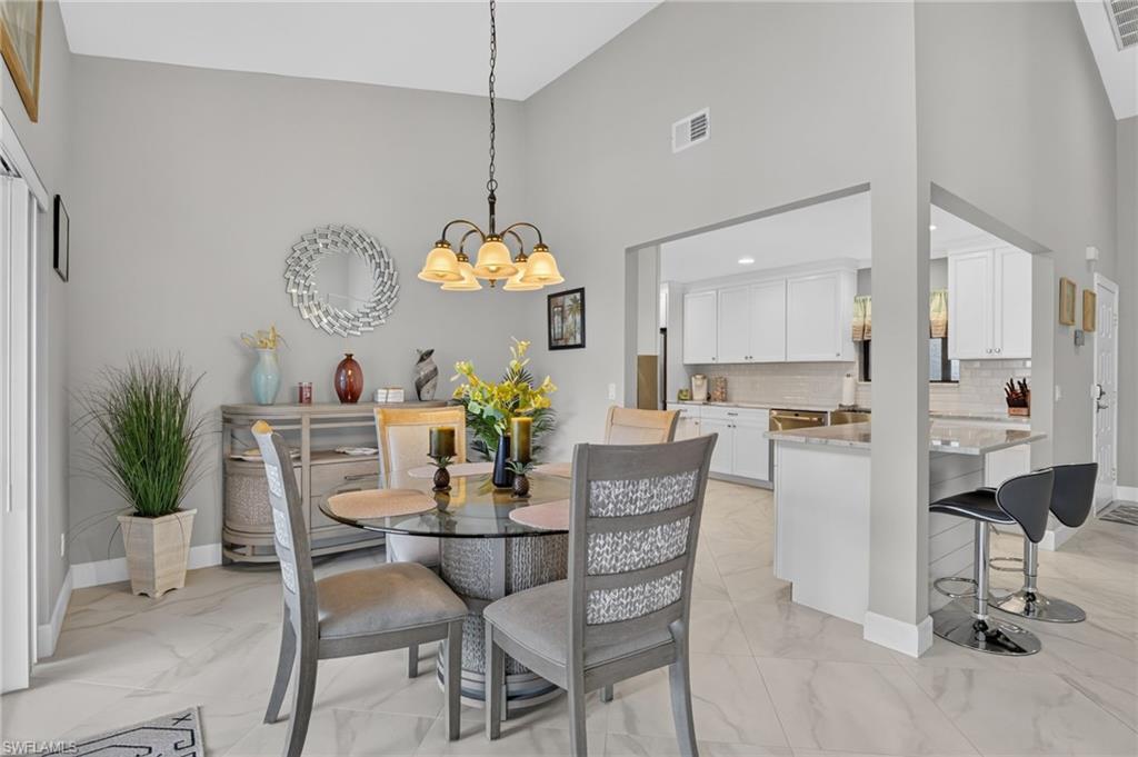 Vaulted ceiling dining area featuring a glass-top table, chandelier, and tile flooring