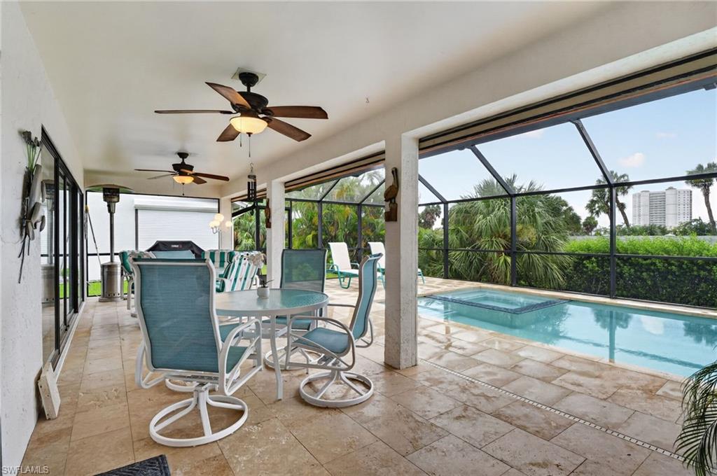 Covered lanai featuring travertine tile flooring, dual ceiling fans, a screened enclosure, a swimming pool, and an integrated spa