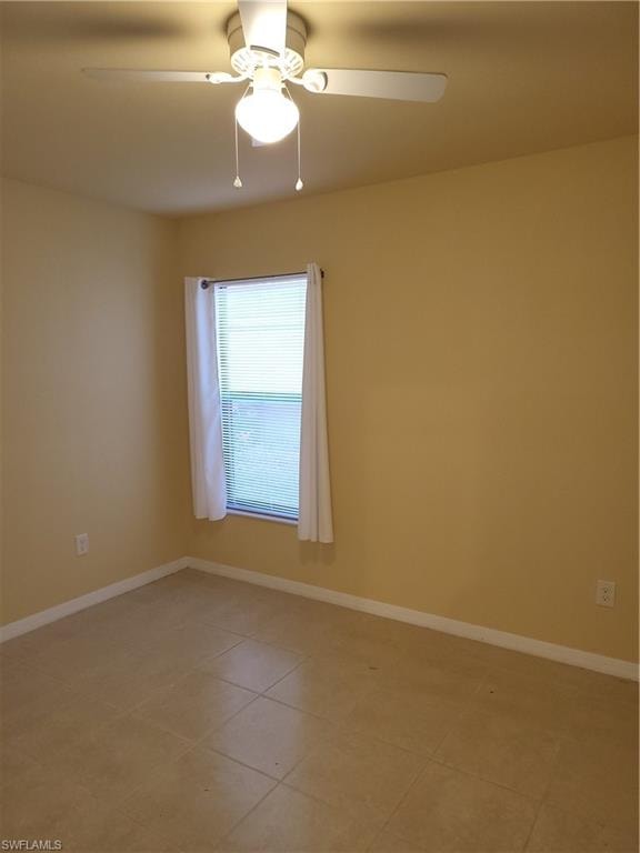 Spare room featuring light tile patterned flooring, a ceiling fan, and baseboards