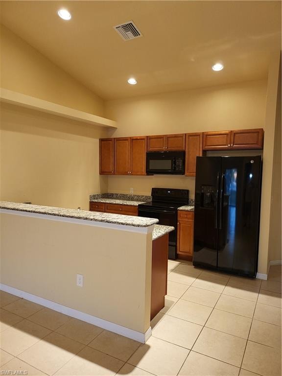 Kitchen with light stone counters, stove, visible vents, fridge, and brown cabinets