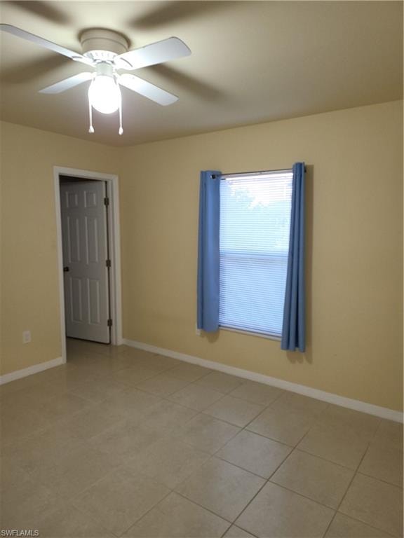 Unfurnished room with light tile patterned floors, a ceiling fan, and baseboards