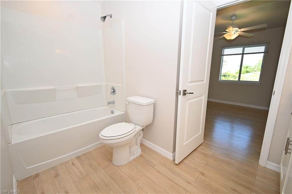 White acrylic tub and shower combination with chrome fixtures, light wood-finish flooring, and a white toilet